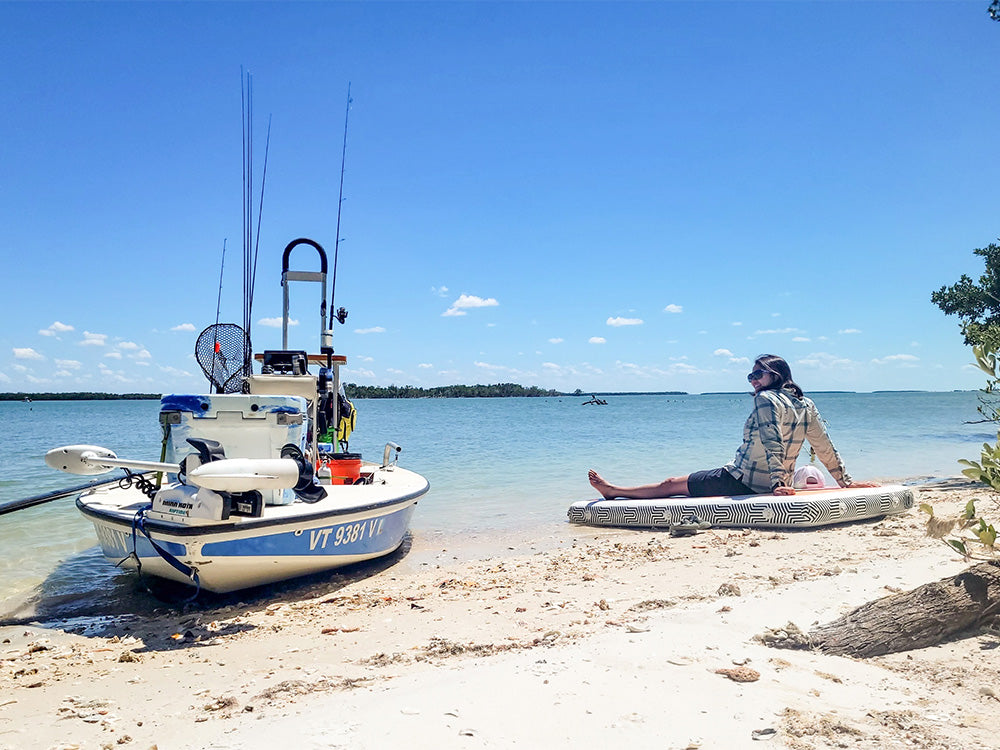 A woman sat on the cambia adaptable inflatable surface on a beach next to a fishing boat