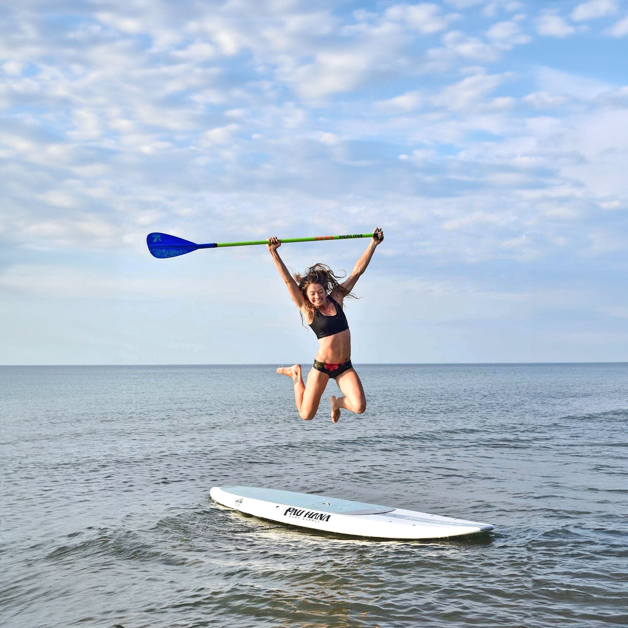 a woman jumping with excitement on a paddleboard holding a paddle in the air