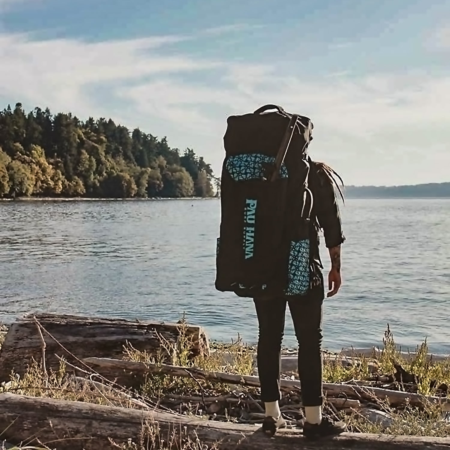 a person stood at a lake front wearing a travel backpack for an inflatable paddleboard