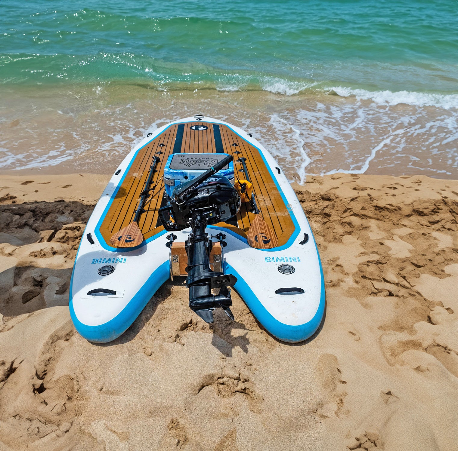 the bimini skiff paddleboard on a beach with a cooler and outboard motor attached