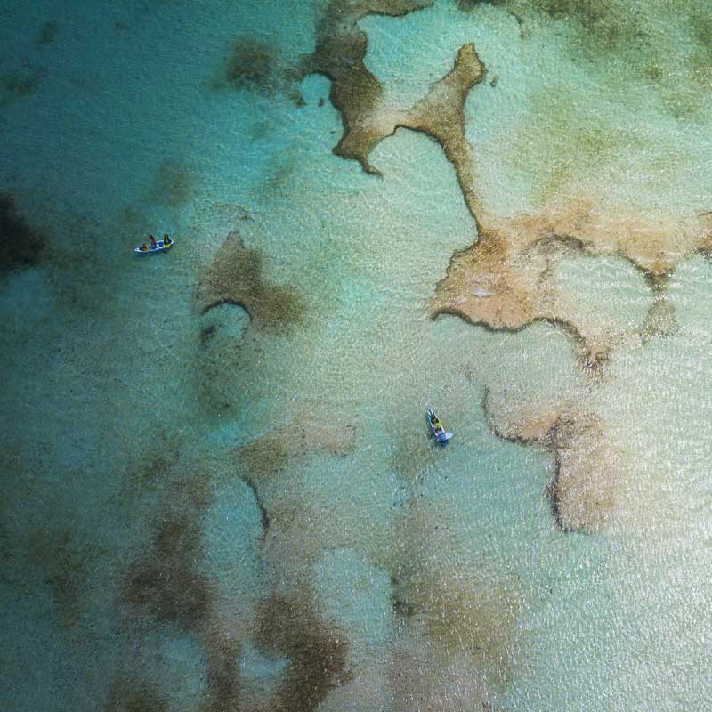 "Aerial view of Pau Hana Surf Supply inflatable paddle boards transporting kiteboarding gear across Barbuda's crystal reef waters, demonstrating the stability of inflatable SUPs"