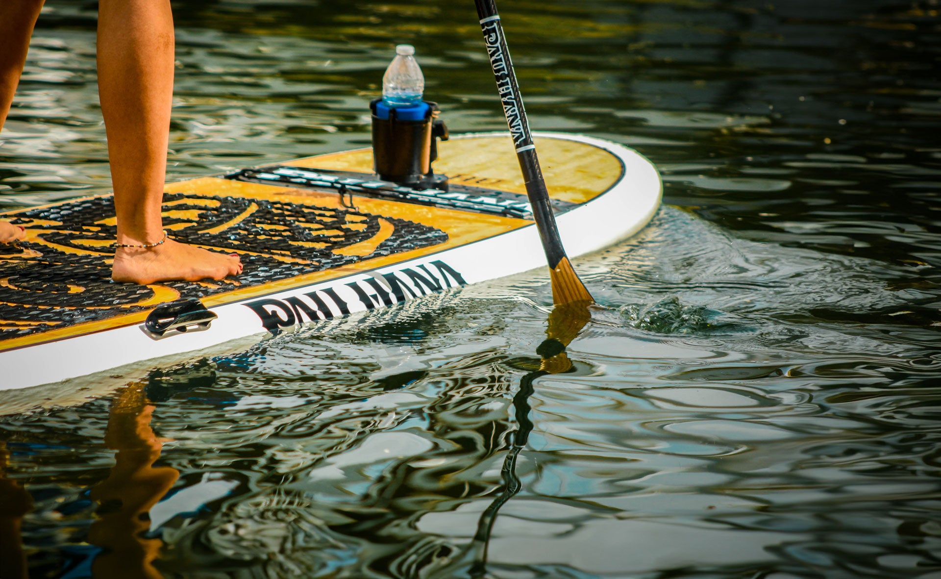 a close up of a person stodd on a paddleboard with a drink holder and paddle in the water