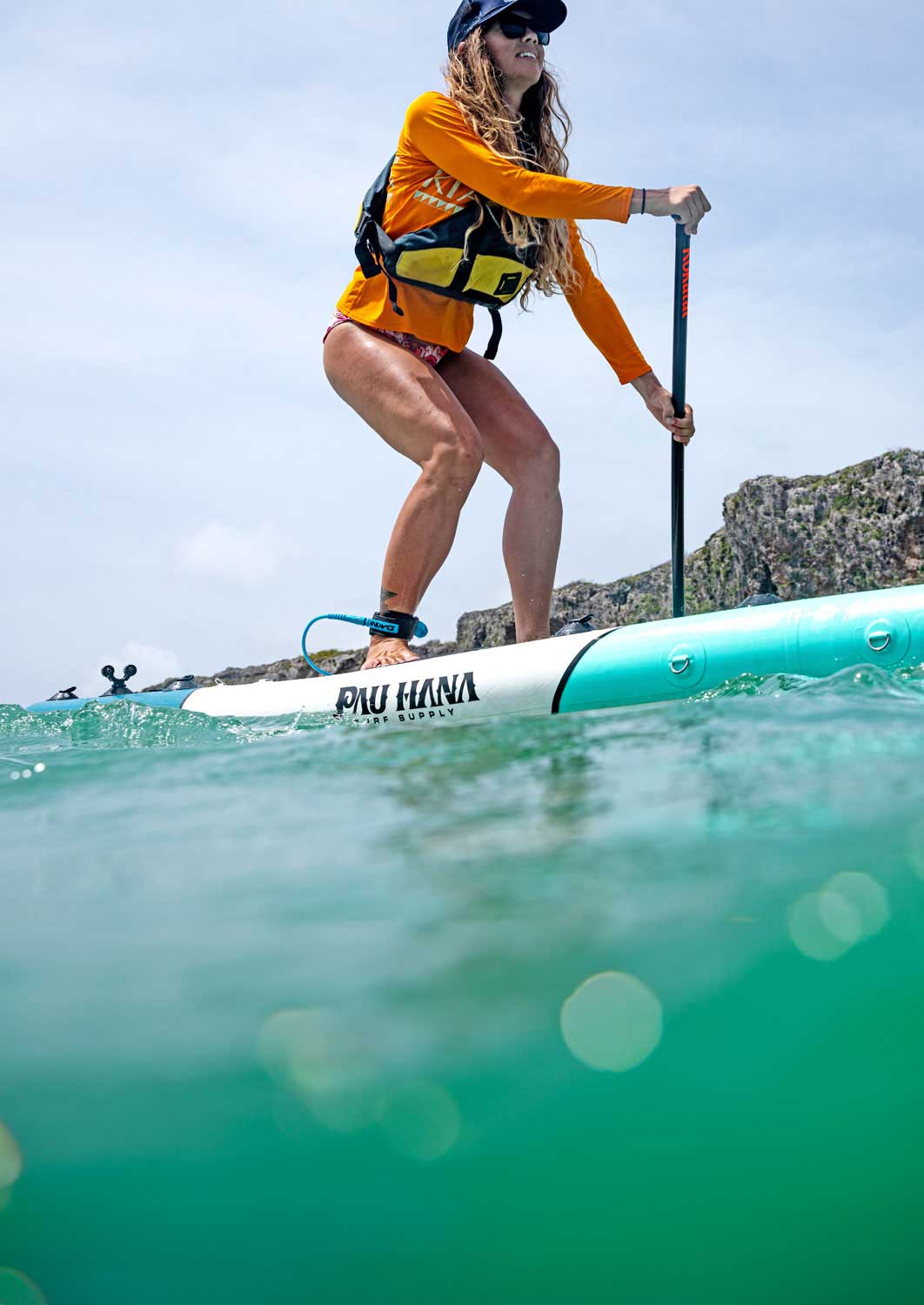 a woman paddling an inflatblae paddleboard on bright turquoise water past some cliffs