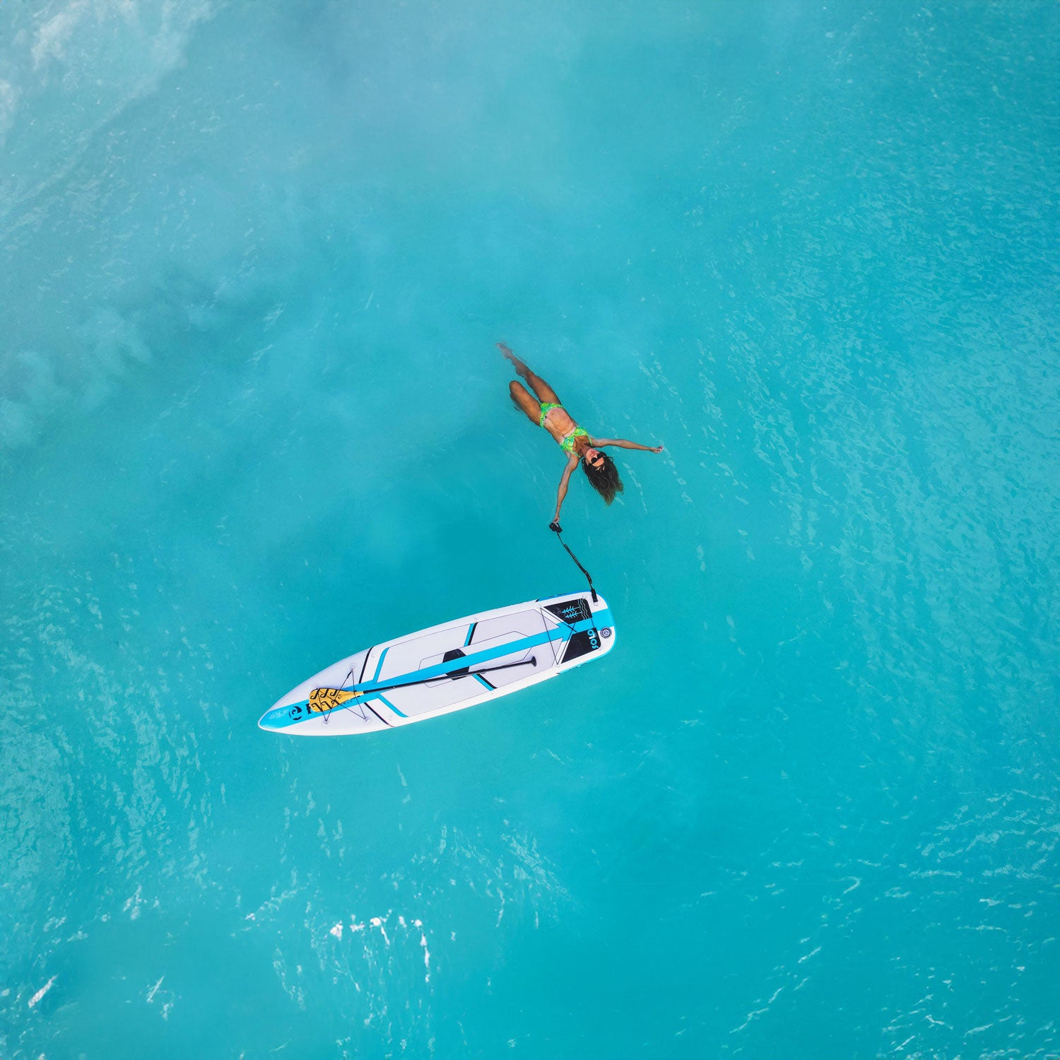 a waoman lying in the blue ocean next to an inflatable paddlebaord