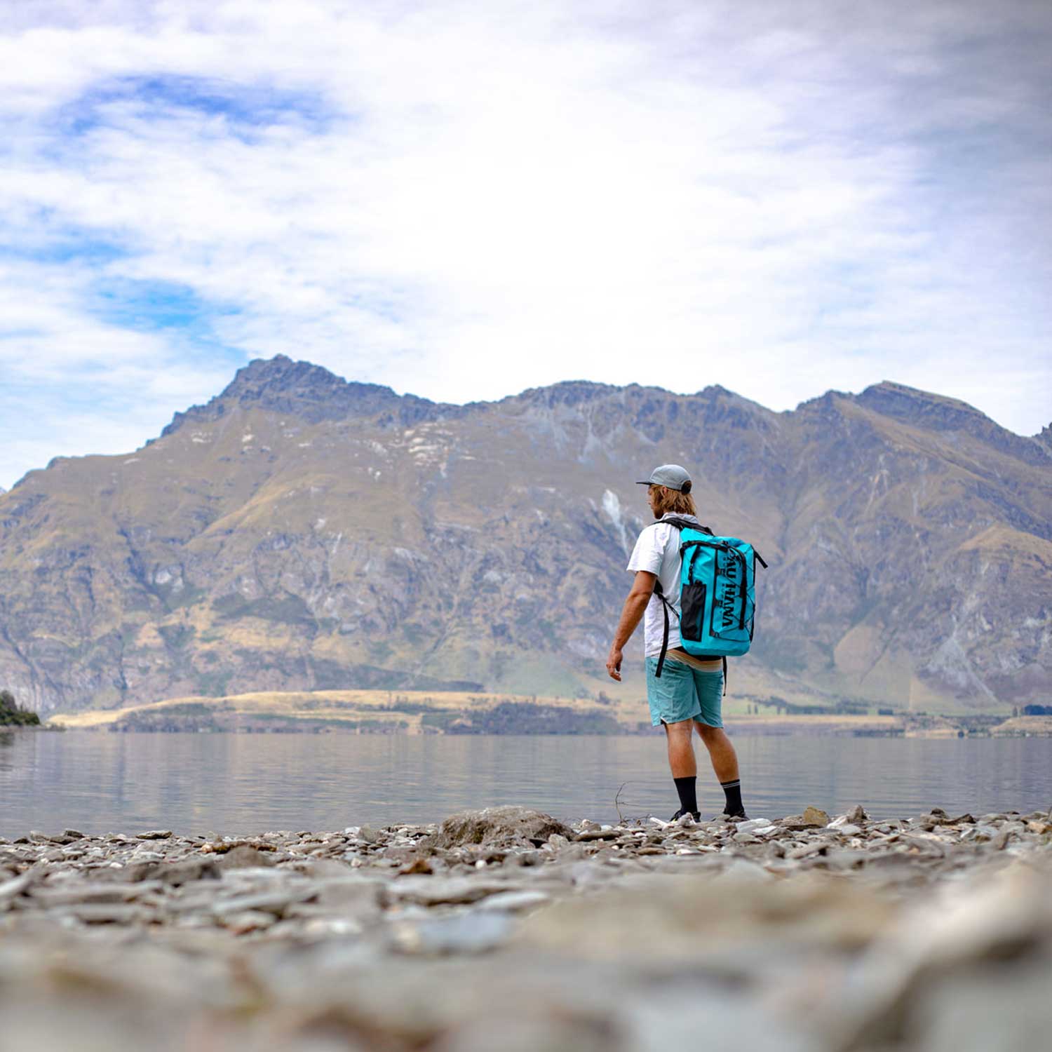 a man looking out over an alpine lake wearing the pau hana solo sup backcountry paddleboard backpack