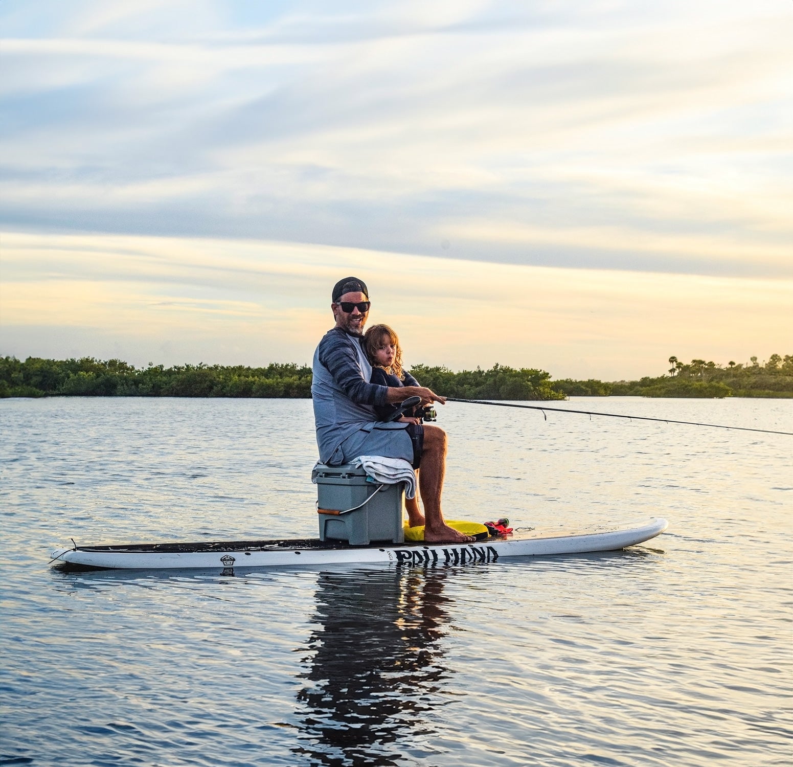 a man and son fishing from a paddleboard at sunset