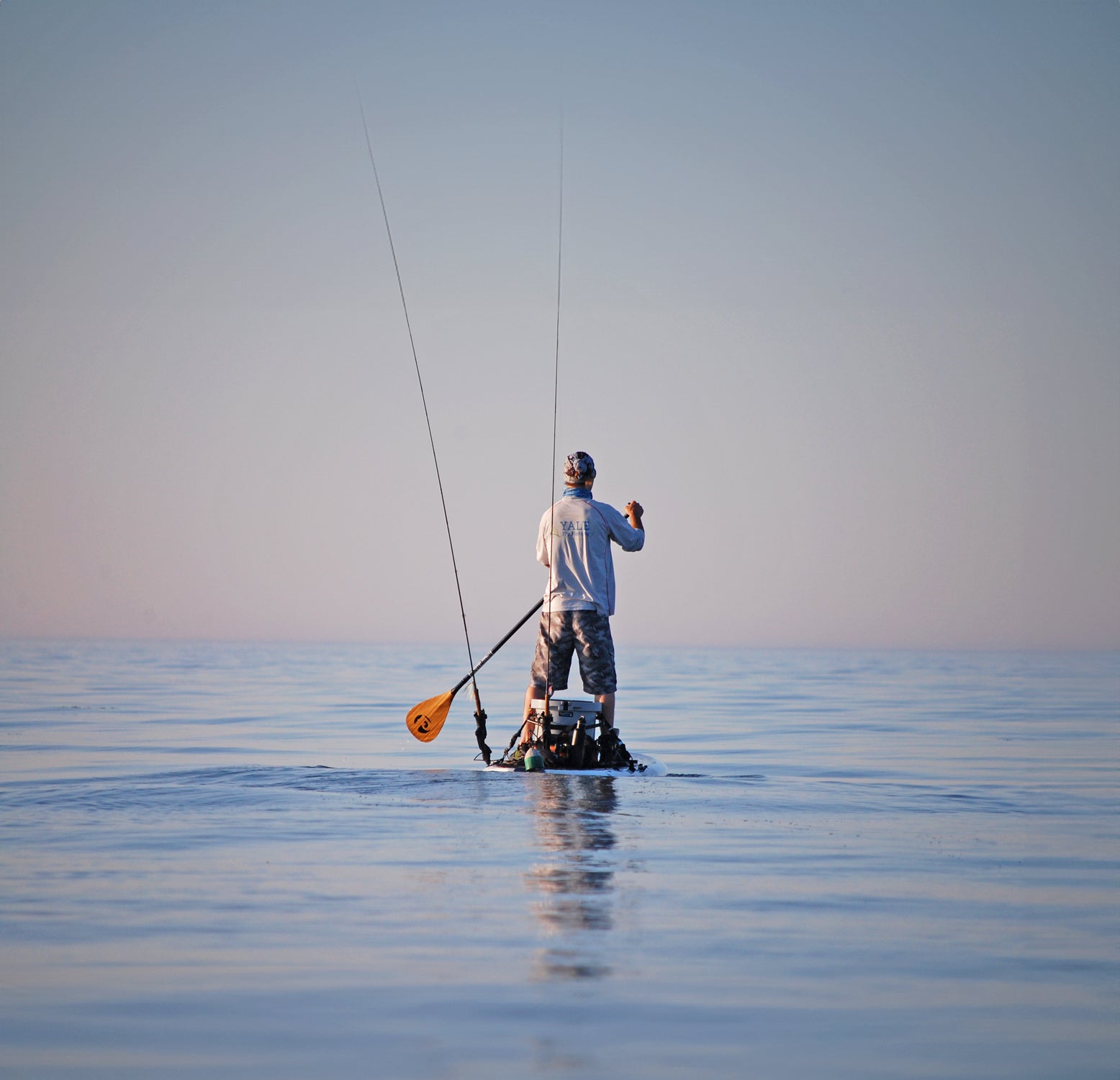 a person paddling a paddleboard rigged with fishing rods