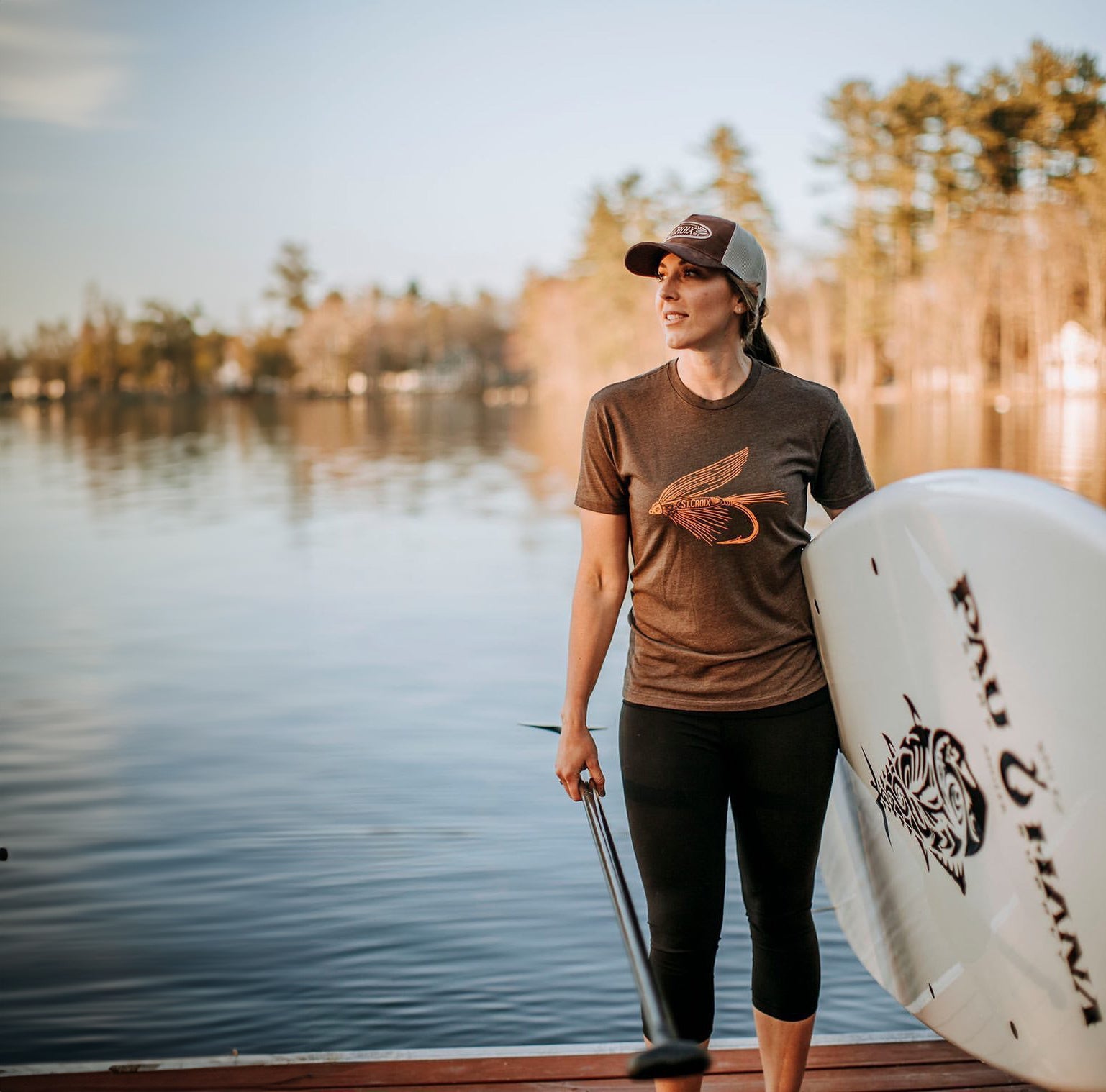 a woman holding a paddleboard next to a lake