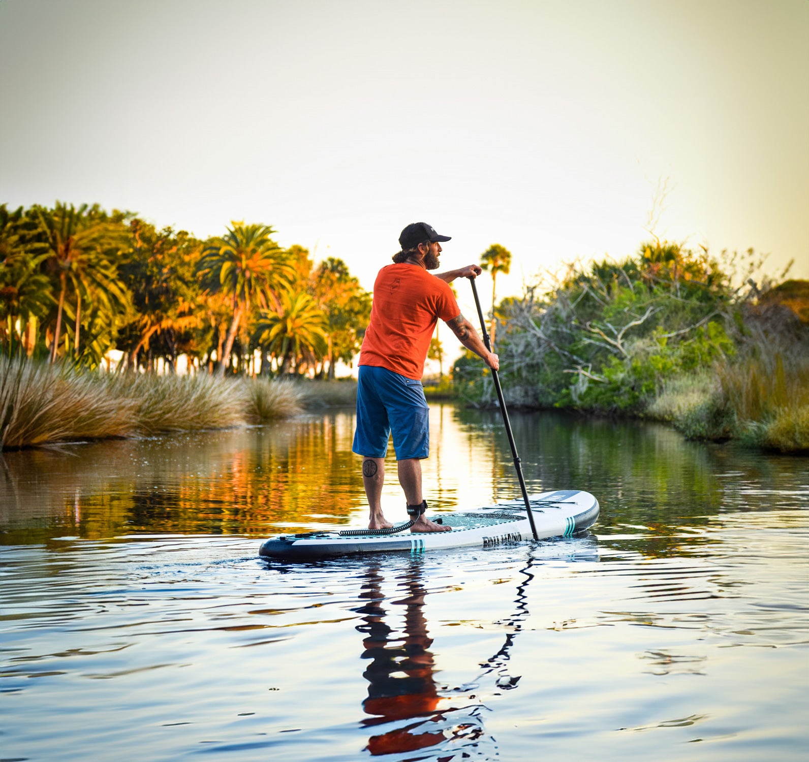 a person paddleboarding at sunset on a body of water lined with palm trees