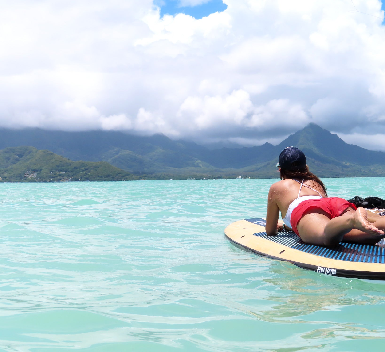 a woman lying on the big ez vft paddleboard on the ocean with mountains and clouds in the background