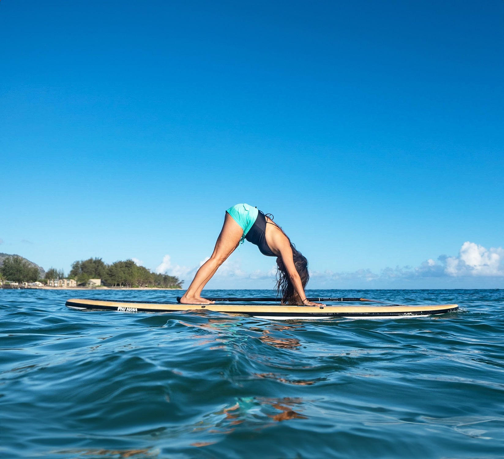 a woman doing yoga on a paddleboard on the ocean with a shoreline in the background