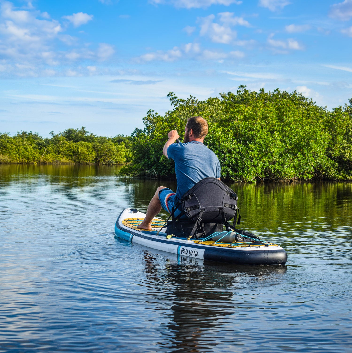 Person on a stand-up paddleboard in a calm body of water with greenery in the background