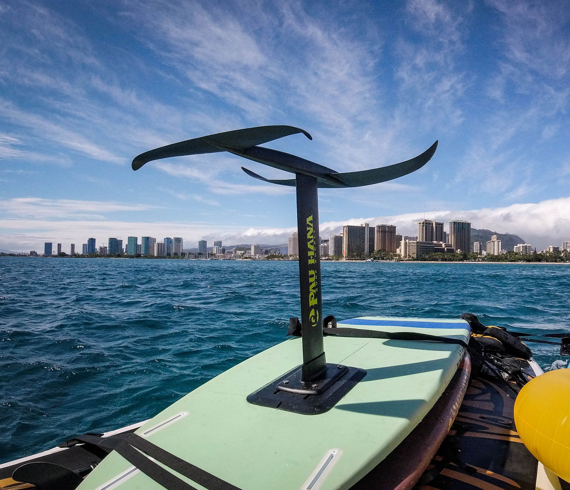 "Pau Hana Surf Supply Stinger wing foil mounted on mint-colored Carve Surf SUP with Honolulu skyline and turquoise waters of Waikiki, showcasing advanced wind sports setup"