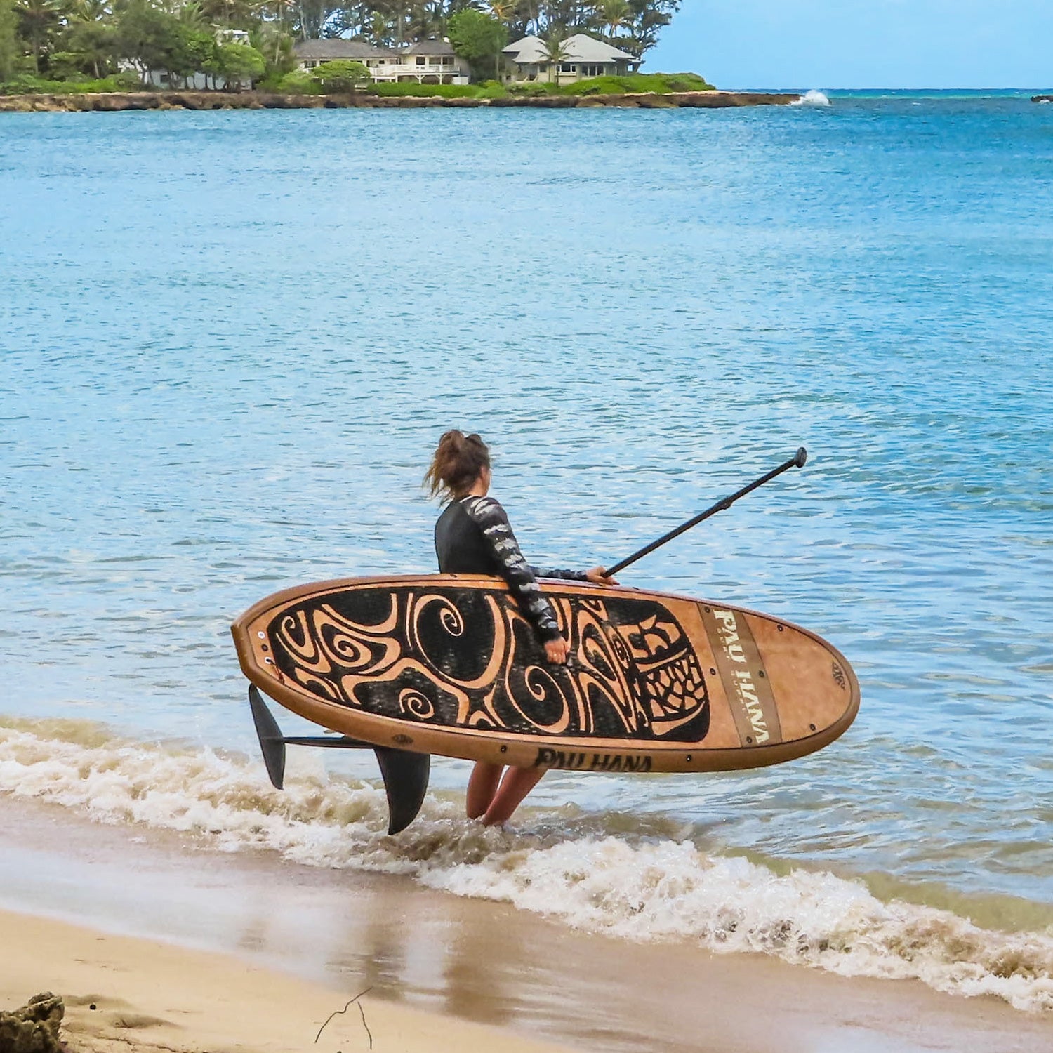 a person walking into the water carrying a stand up paddleboard and paddle