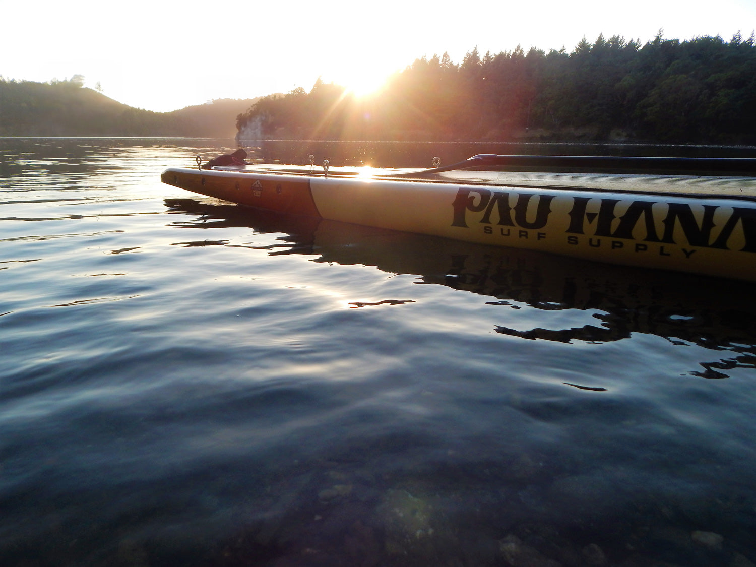 a paddleboard on the water at sunset with trees in the background