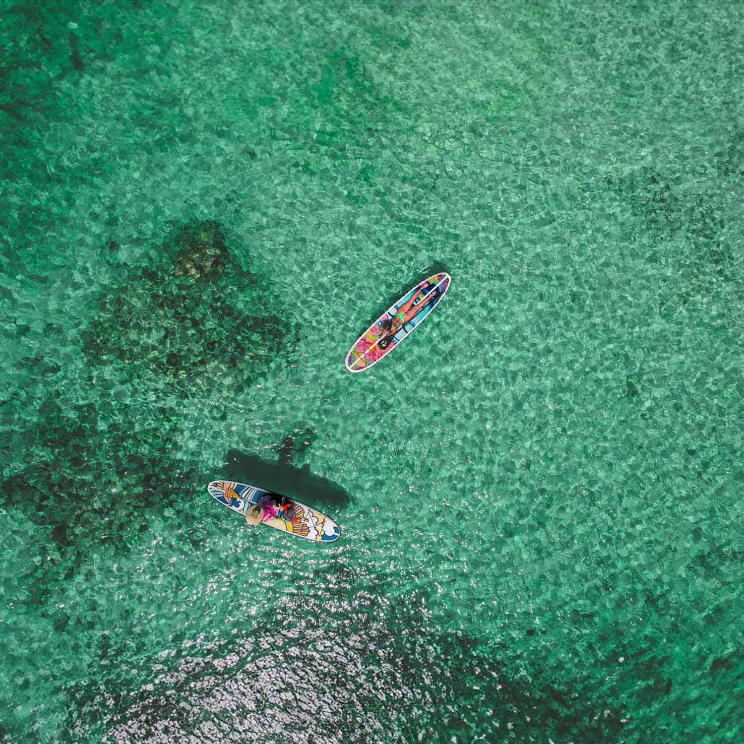 an aerial image of two colorful pau hana stowaway lite paddleboards on bright green ocean