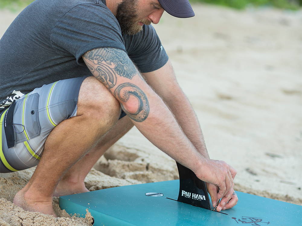 A man screwing a fin into a stand up paddleboard