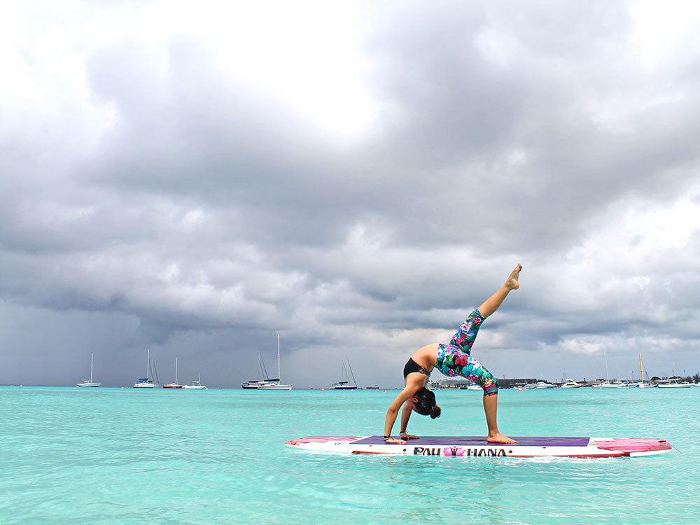 A woman doing yoga on a stand up paddleboard with sail boats in the background