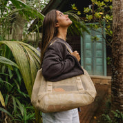 Woman holding a beige tote bag with plants and a wooden structure in the background