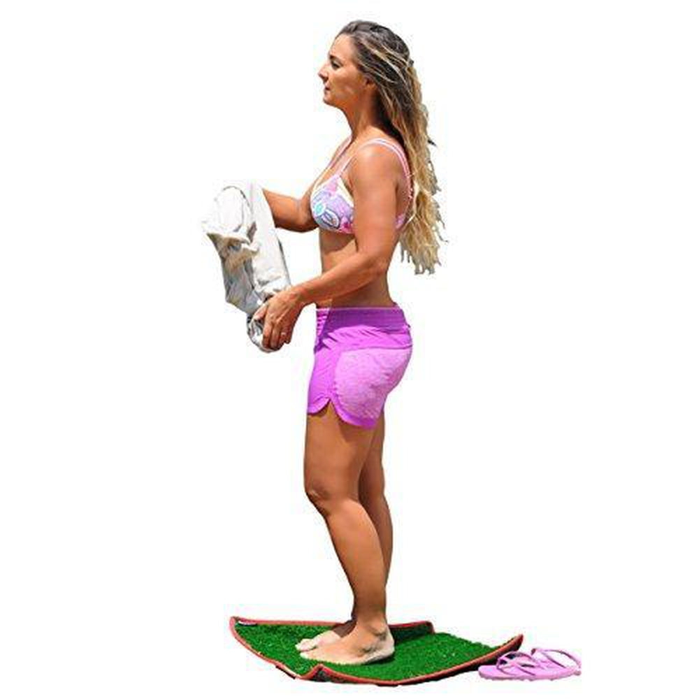 Woman standing on a changing mat with a towel, wearing a pink sports bra and shorts, on a white background.
