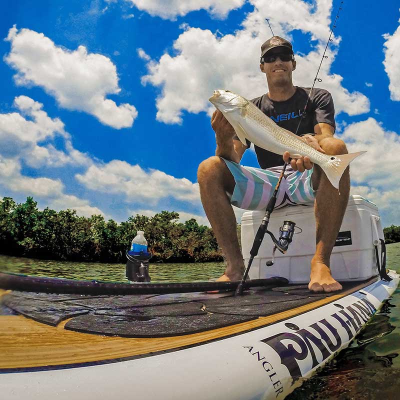 "Successful redfish catch displayed on Pau Hana Surf Supply Angler fishing SUP, showcasing comfort deck pad, cooler and tackle in Florida mangroves"