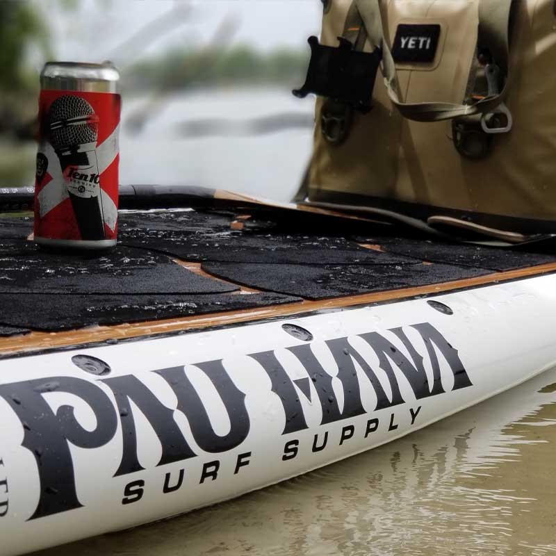 A beer and a dry bag on the Pau Hana Surf Supply Big EZ Angler fishing paddleboard floating on the water