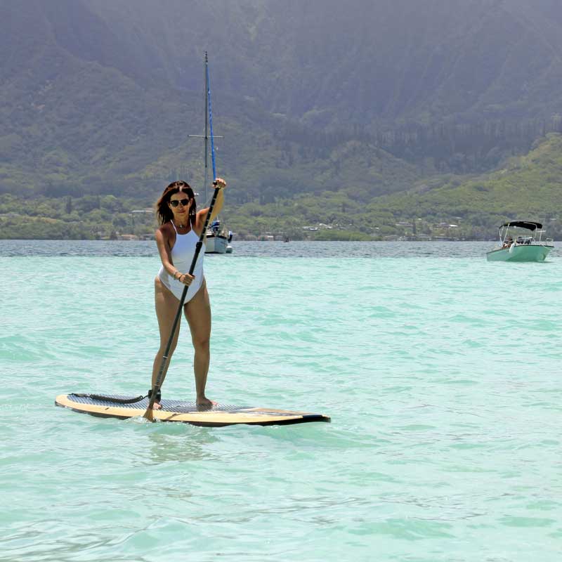 "Pau Hana Surf Supply paddler in Kaneohe Bay, Hawaii, showcasing the stability of the 11'0" Big EZ Hawaiian VFT Wood board on turquoise waters, Ko'olau mountains backdrop"