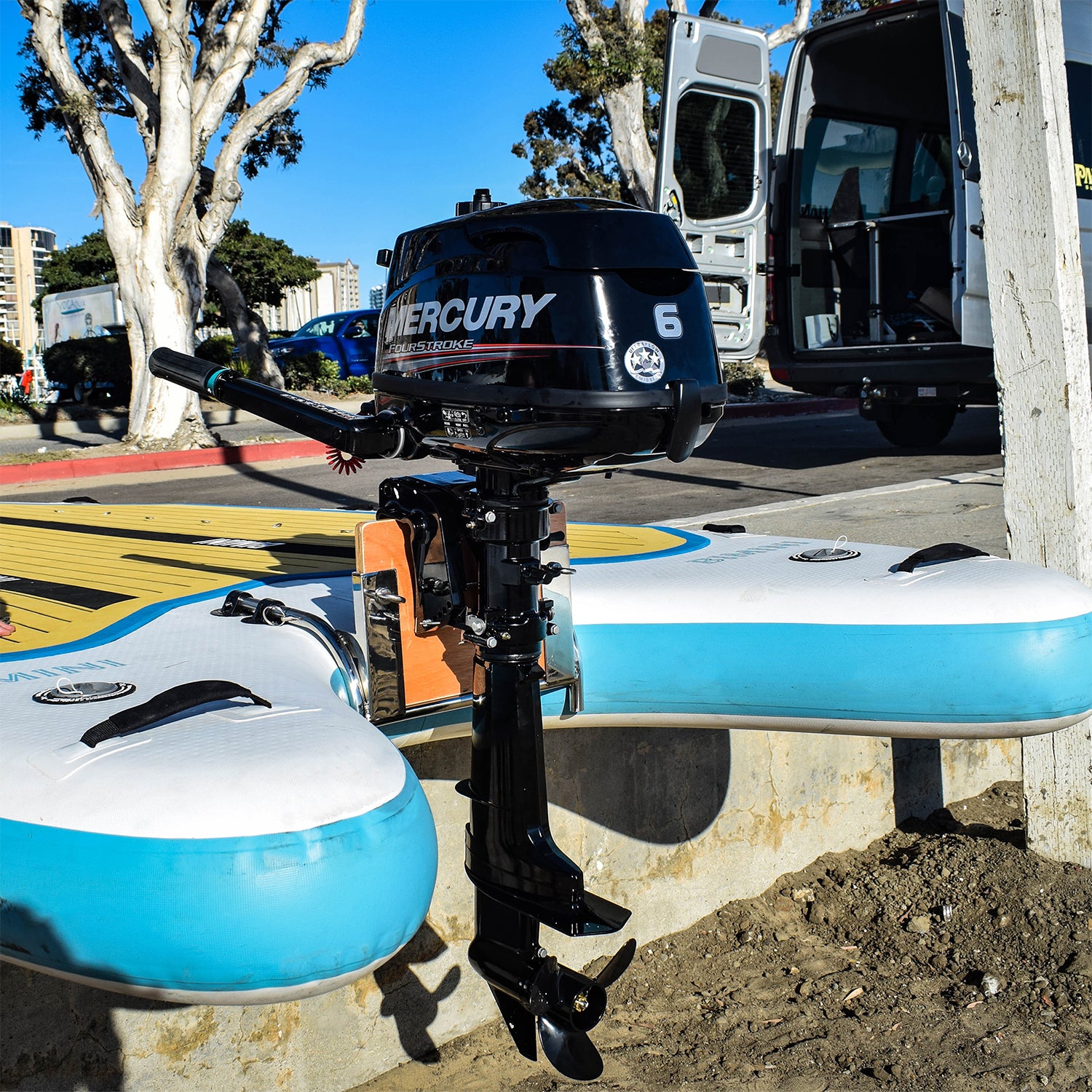 A 5hp motor attached to a Pau Hana Surf Supply Bimini Skiff inflatable paddleboard on the pavement with a van in the background