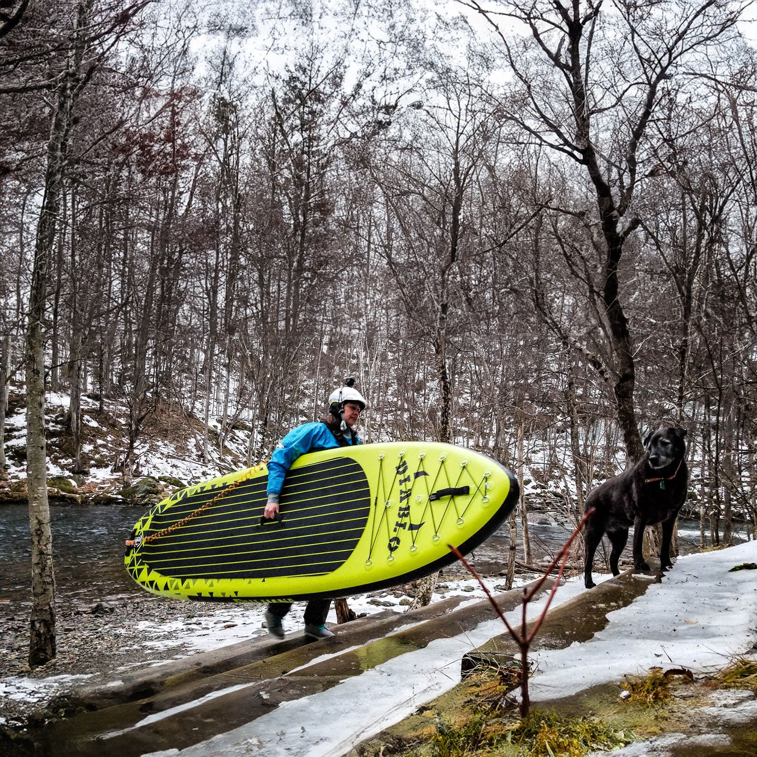 Pau Hana Surf Supply Diablo Air whitewater inflatable paddleboard being carried up snowy stairs with a dog