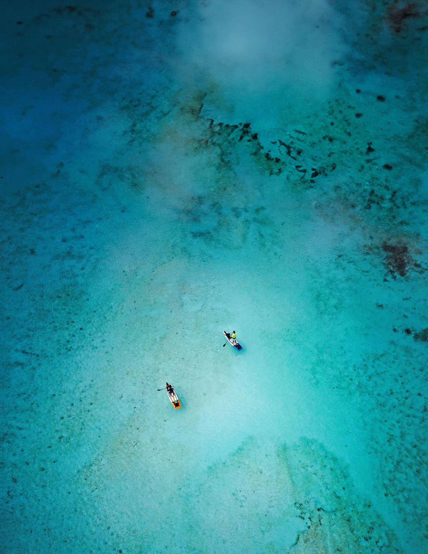 "Aerial view of two paddlers on Pau Hana Surf Supply Endurance Air touring SUPs exploring Caribbean turquoise waters and coral reefs during island adventure"