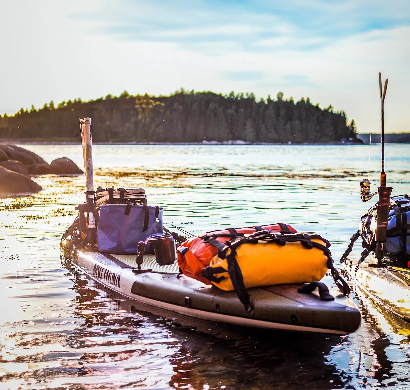 A paddleboard on the water loaded with gear by a dock with an island in the background