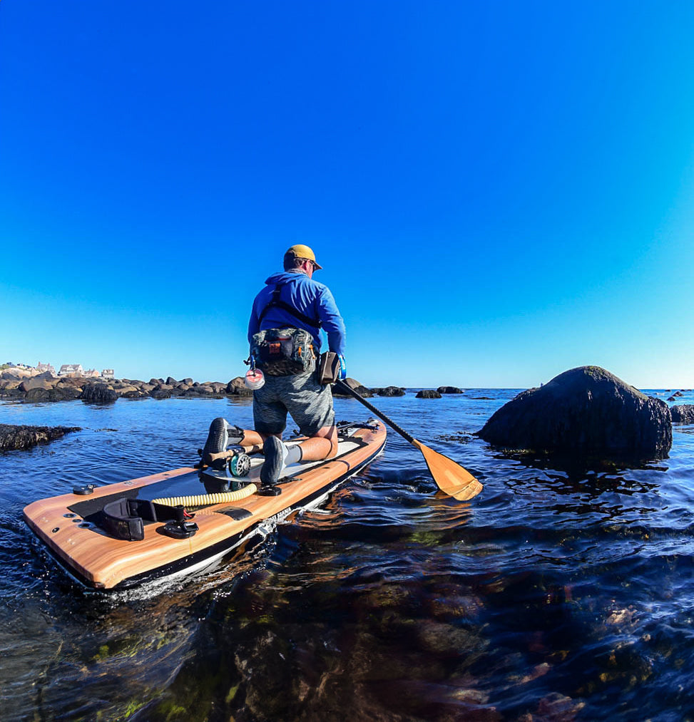 "Pau Hana Surf Supply Endurance VFT touring paddleboard with fly rod on EVA deck pad navigating rocky coastal waters"