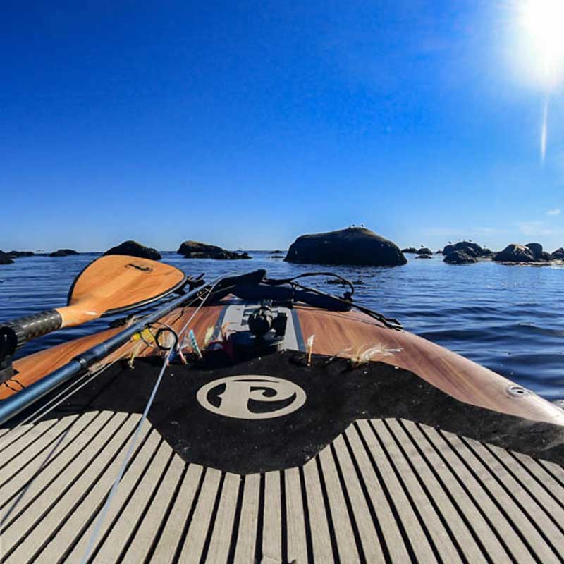 A close up of the EVA deck pad on the Pau Hana Surf Supply 12'0" Endurance VFT touring paddleboard on a lake with a fly rod and flies