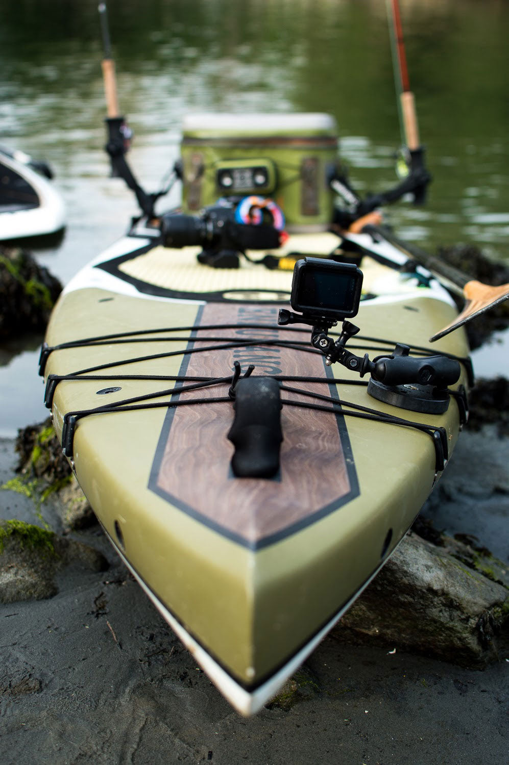 "Pau Hana Surf Supply Endurance touring SUP rigged for fishing with mounted GoPro, rod holders and deck storage, bow view showing olive design"