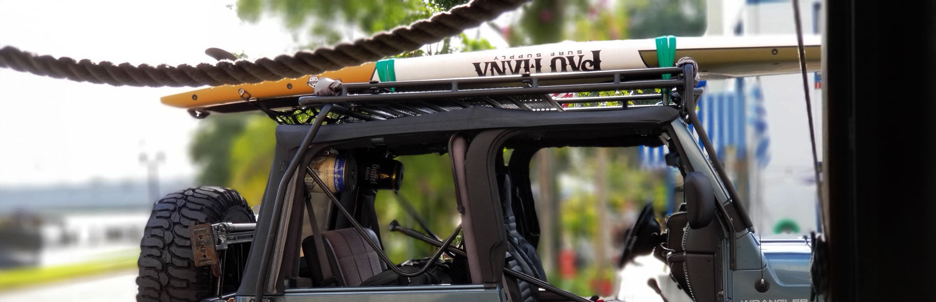 "Pau Hana Surf Supply Endurance SUP board mounted on Jeep rack, Florida adventure-ready transport setup with off-road tires"