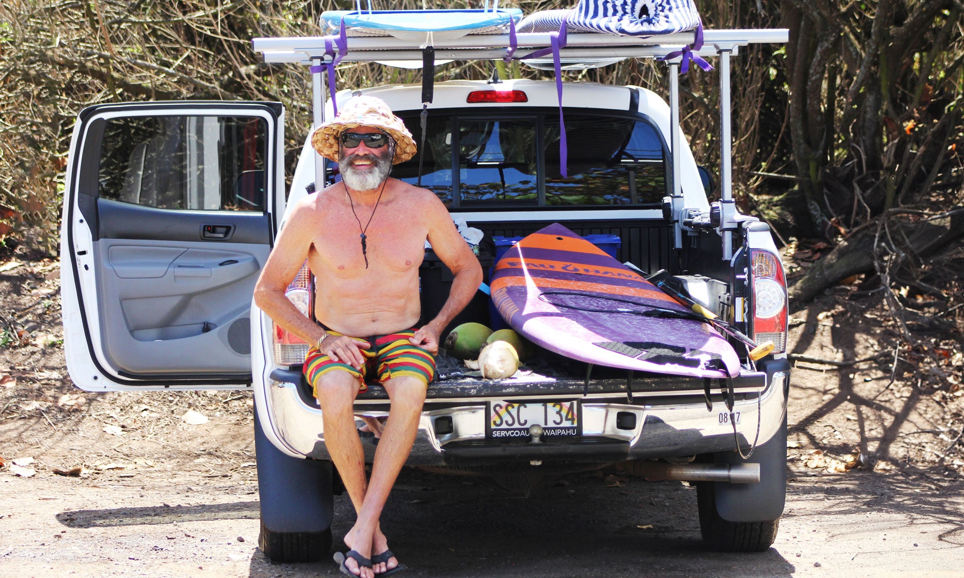"Pau Hana Carve Performance SUP Surf board loaded in white pickup truck with custom aluminum rack system, tropical beach setup"