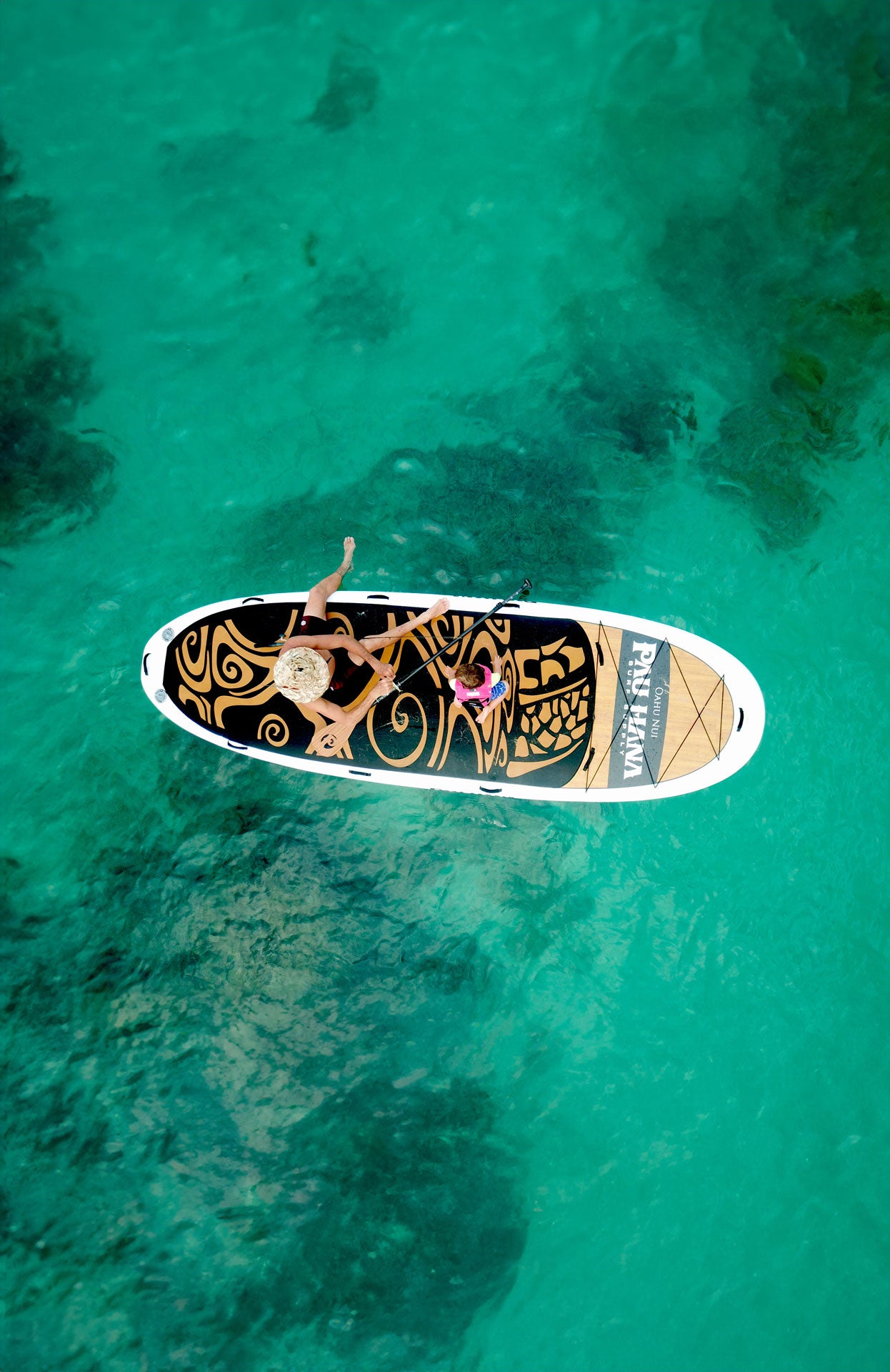 "Aerial view of parent and child lounging on a Pau Hana Surf Supply Oahu Nui giant inflatable family paddleboard in turquoise ocean"