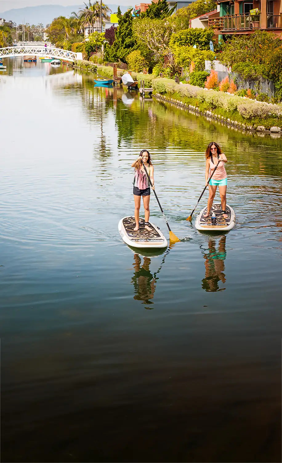 Two people paddleboarding on a calm waterway with a scenic background.