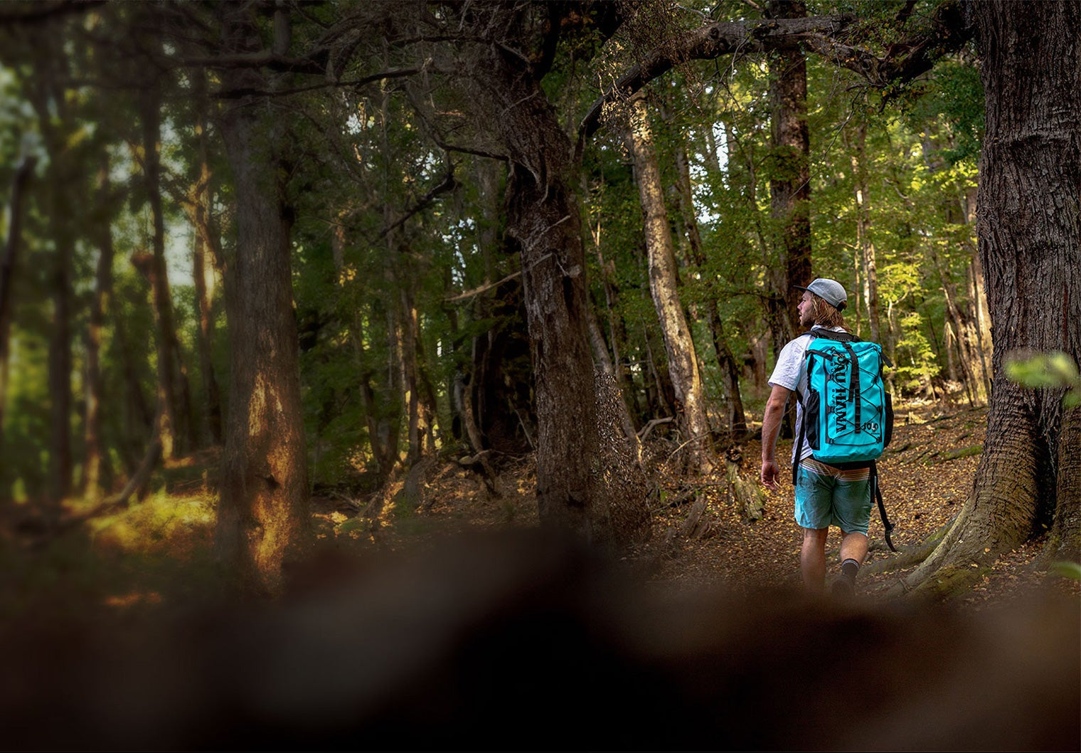 "Pau Hana Solo SUP dry bag backpack in forest trail setting, showcasing portable inflatable paddleboard transport for backcountry access"