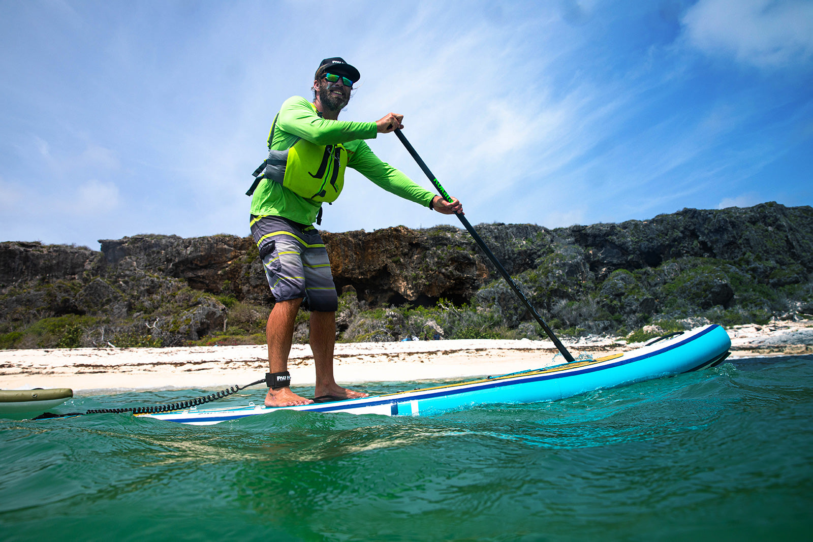 "Pau Hana Surf Supply Calypso inflatable SUP in azure waters, paddler in hi-vis gear navigating coastal cliffs on turquoise sea"