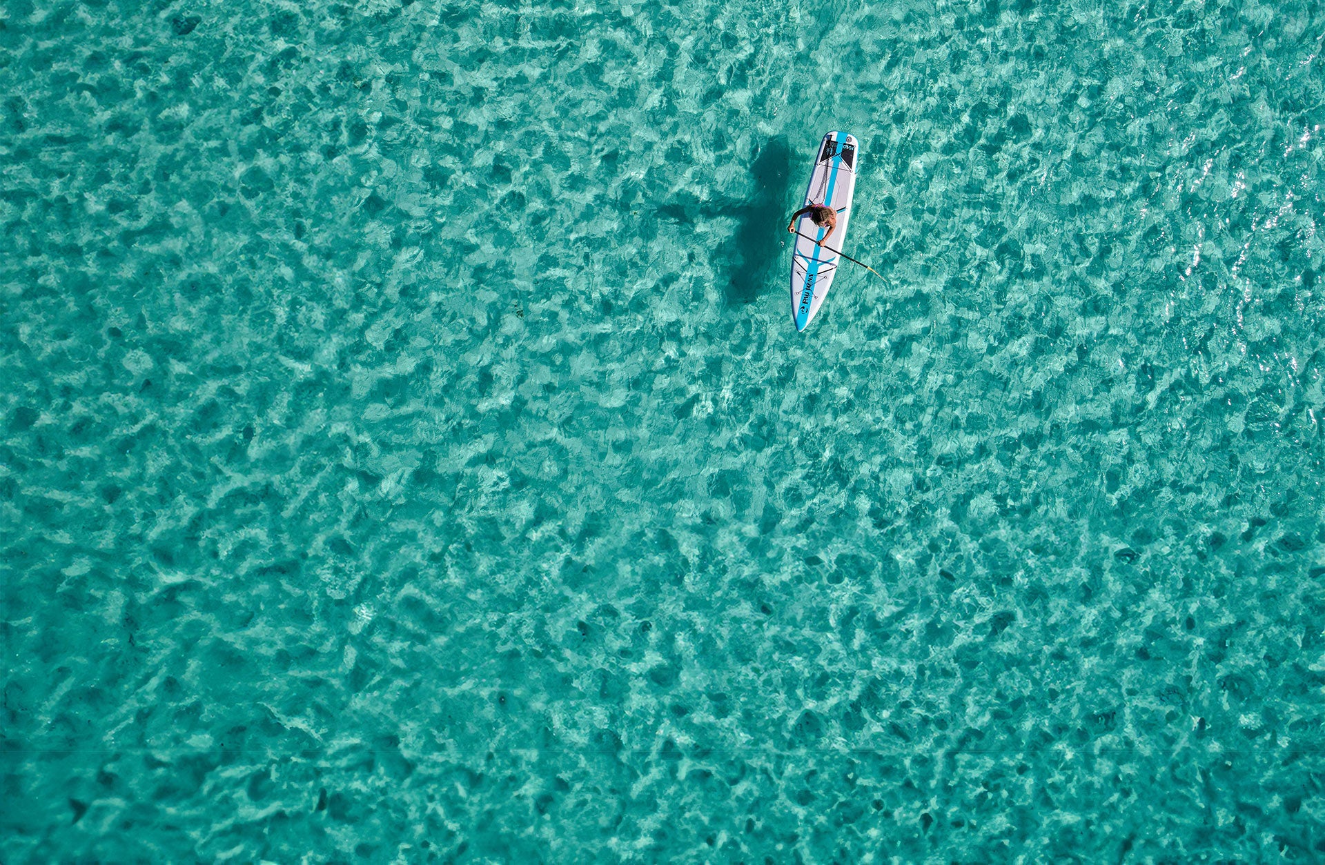 "Aerial drone shot of Pau Hana Surf Supply  Solo SUP backcountry board gliding through crystal-clear turquoise waters, showcasing stability and tracking performance"