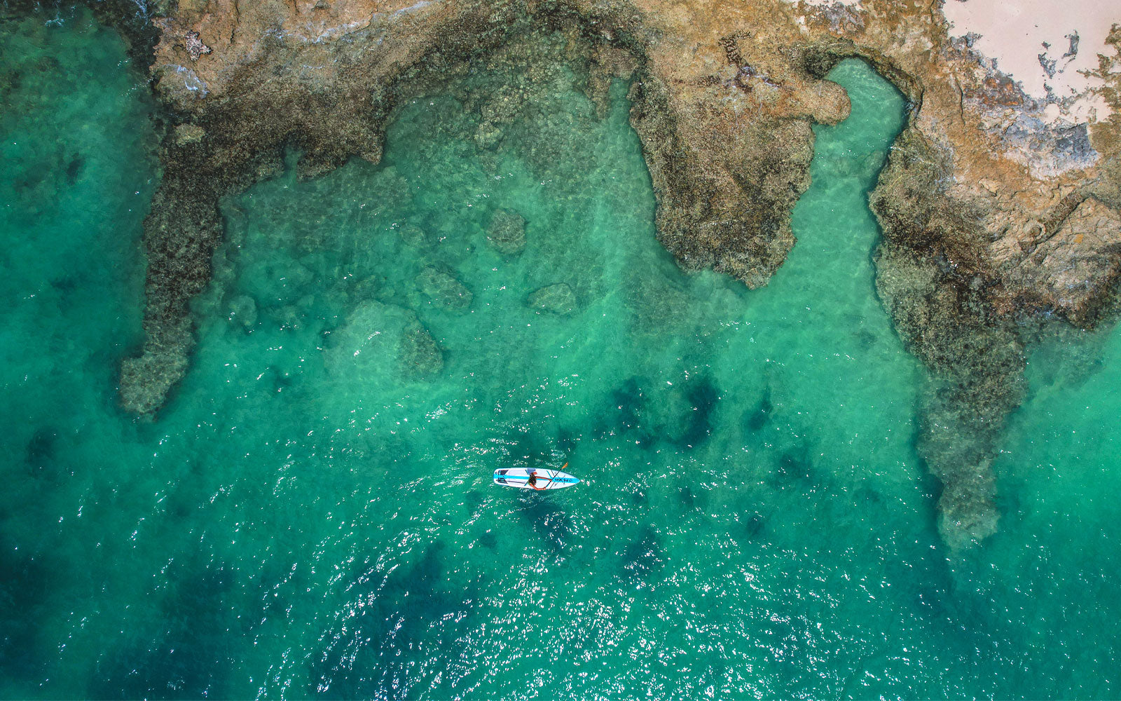 "Aerial drone shot of Pau Hana Surf Supply Solo SUP backcountry board gliding on the coastline in Barbuda waters, showcasing stability and tracking performance"