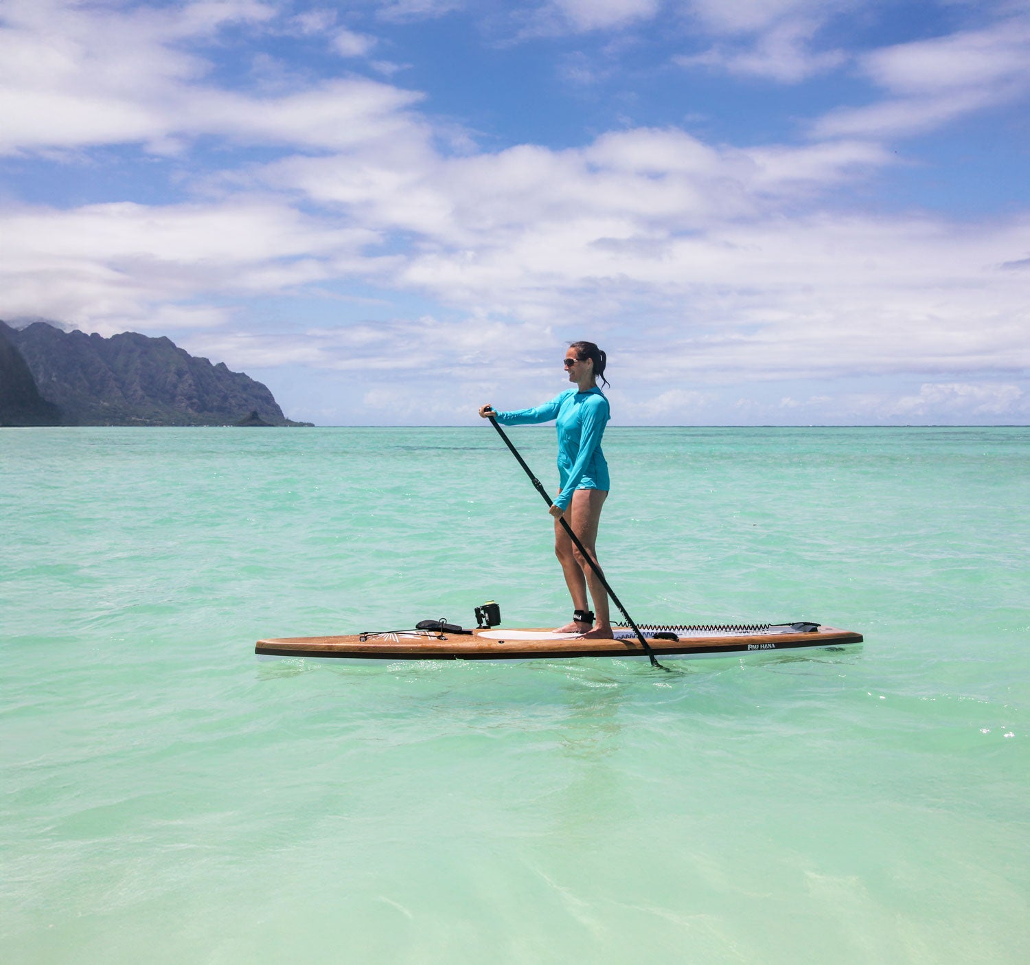 Person paddleboarding on clear turquoise water with a mountainous island in the background