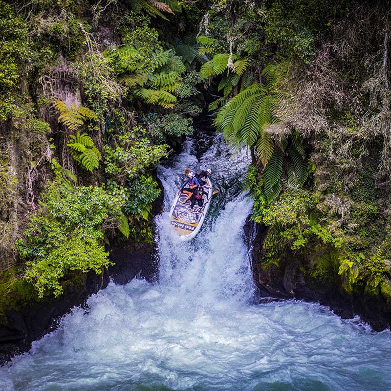 Pau Hana Surf Supply Oahu Nui giant inflatable family paddleboard going over a waterfall surrounded by new zealand native bush wearing safety equipment for whitewater paddling