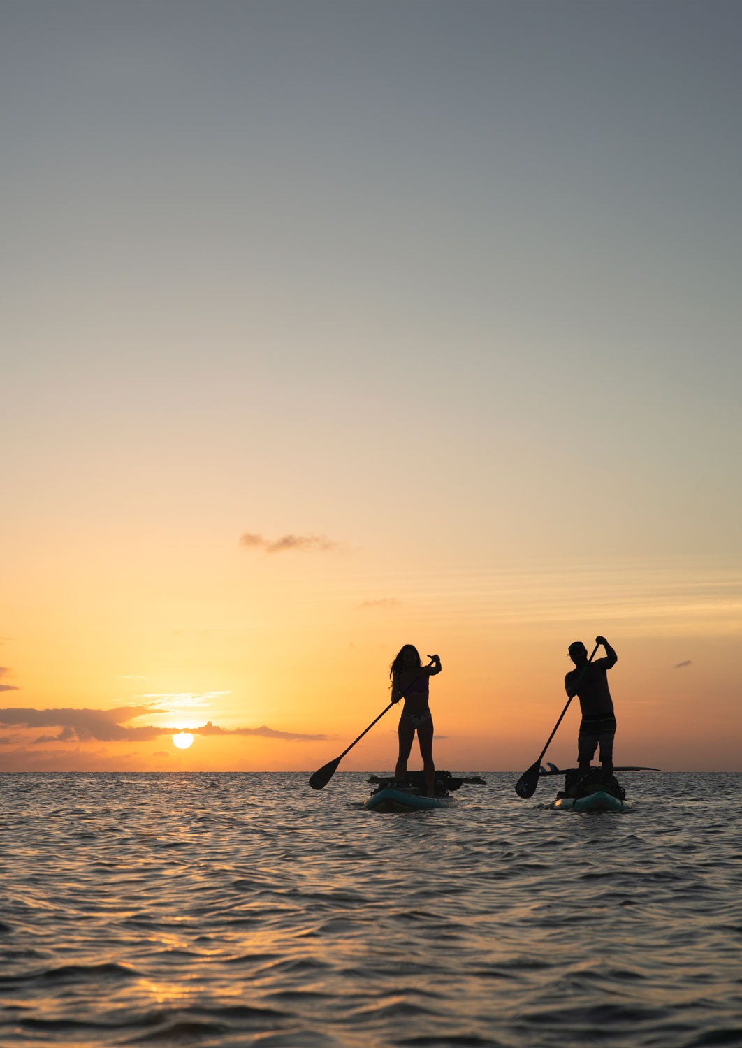 "Silhouetted paddlers on Pau Hana Surf Supply Endurance touring boards returning to shore at golden sunset"