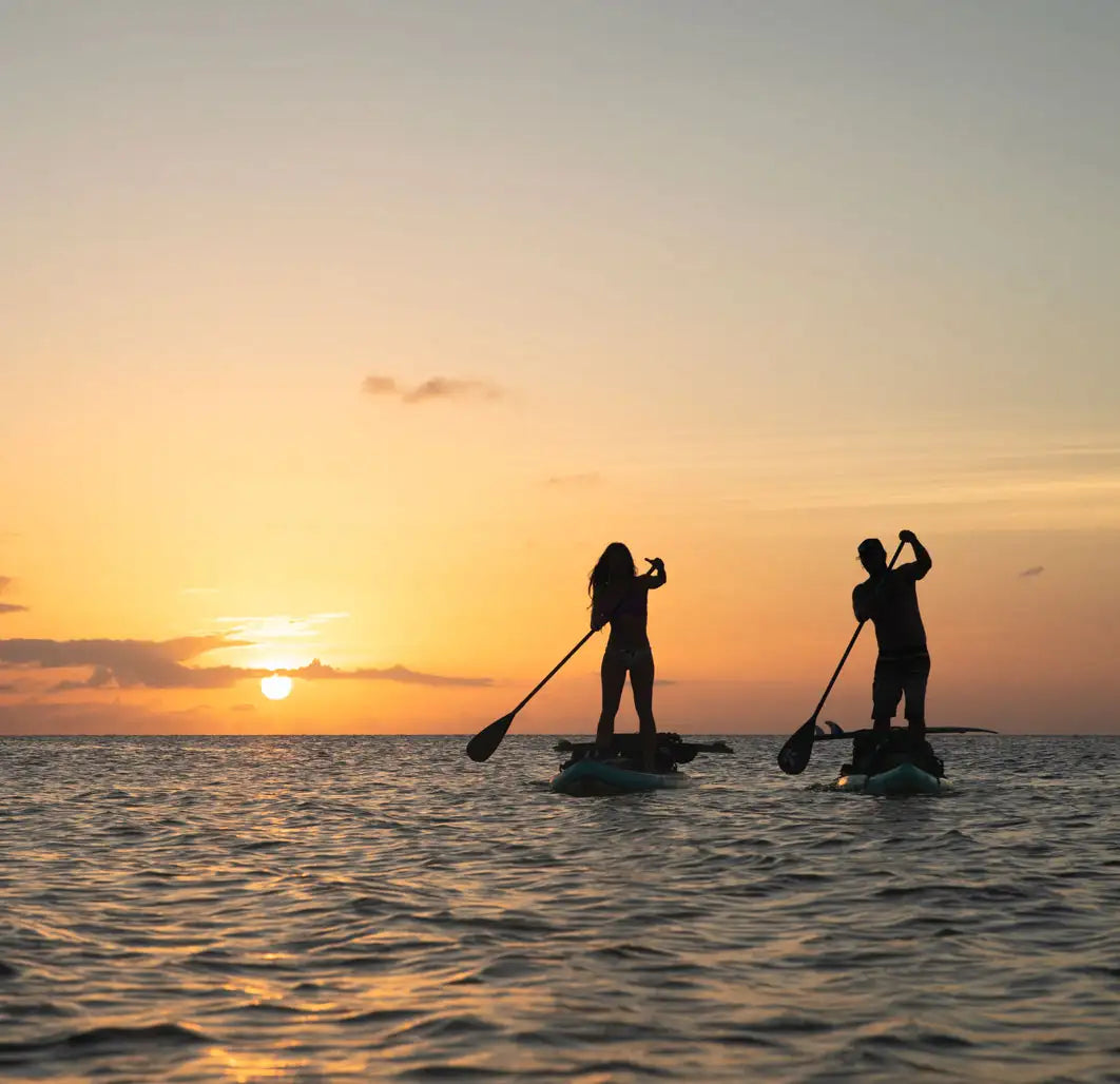 Two people paddleboarding at sunset on a calm body of water.