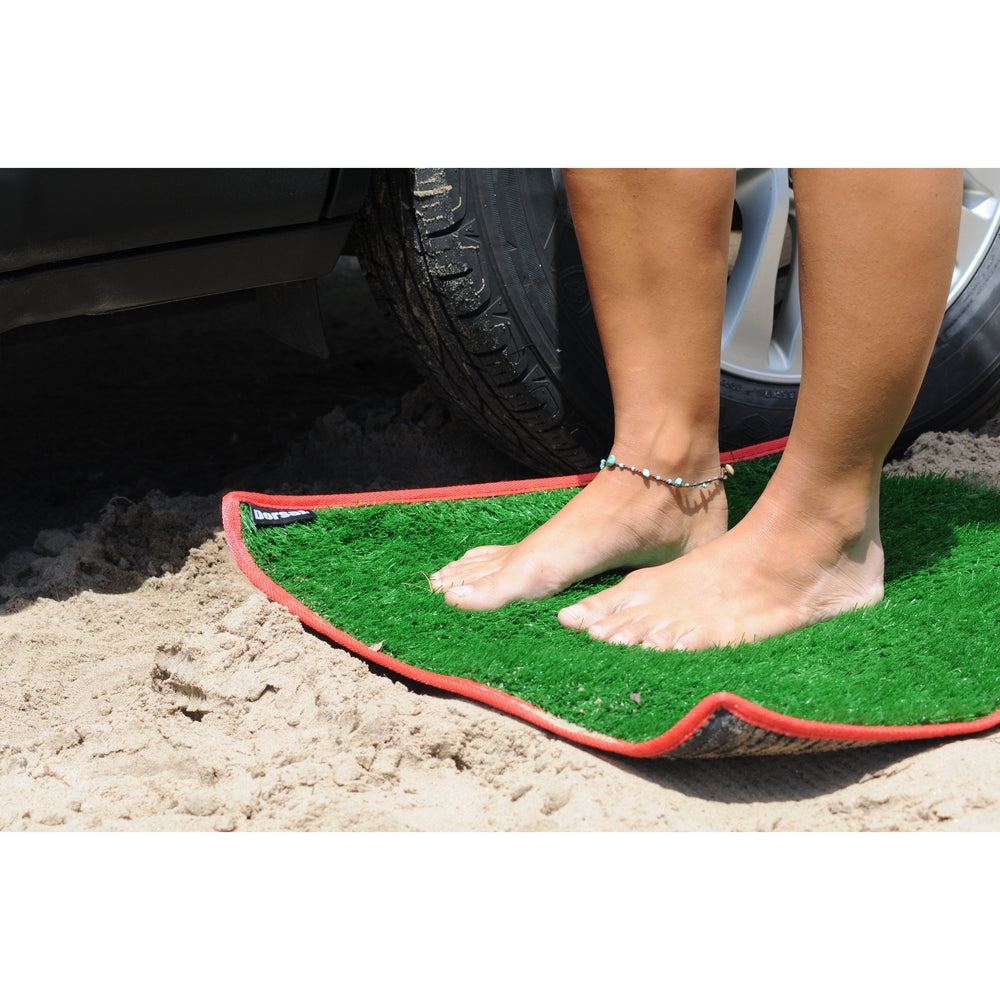 Green grass-like mat with red border on sand, person standing on it.