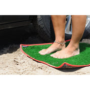 Green grass-like mat with red border on sand, person standing on it.