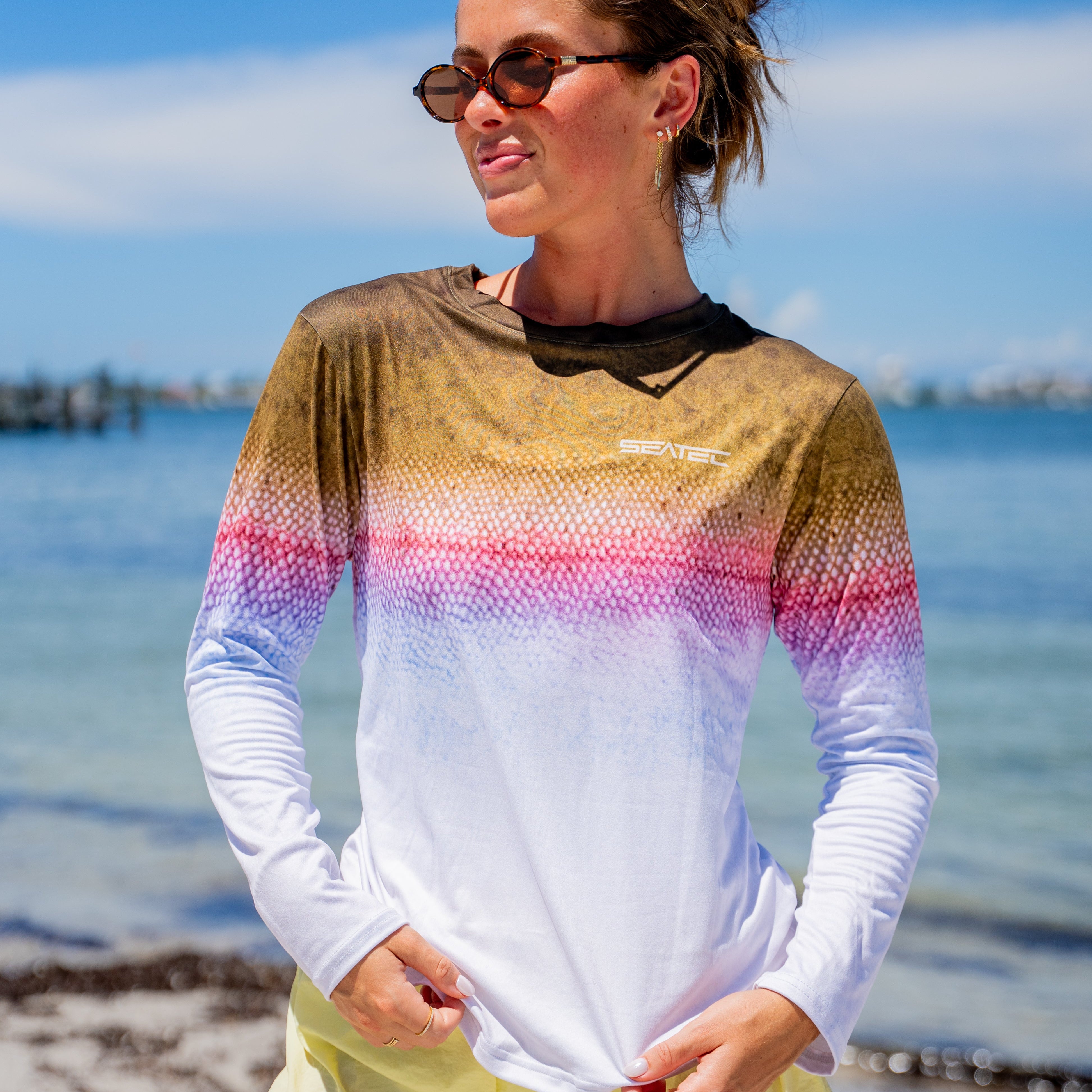 Woman wearing a colorful long-sleeve shirt and yellow shorts on a beach.