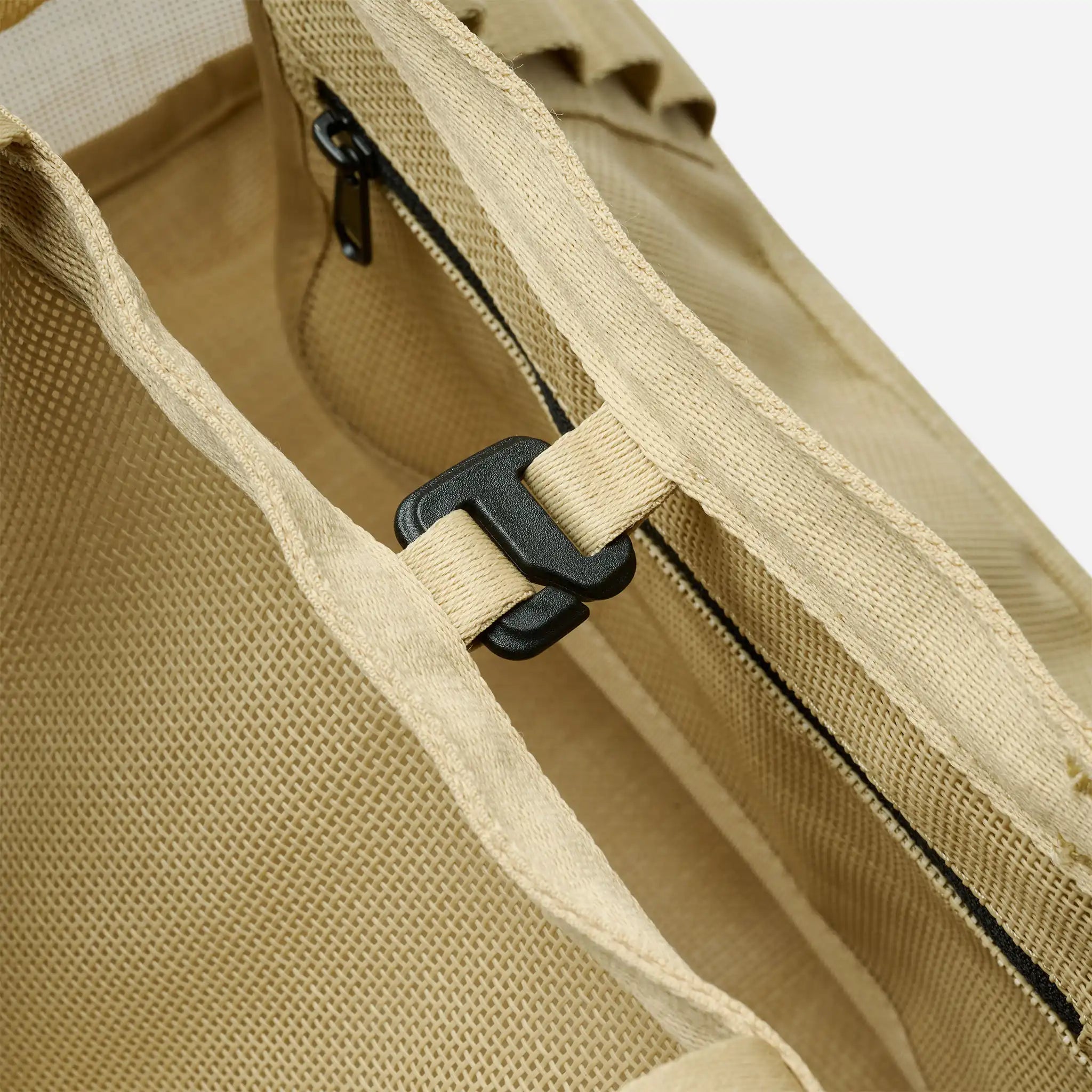 Close-up of a beige bag with a black zipper and strap.